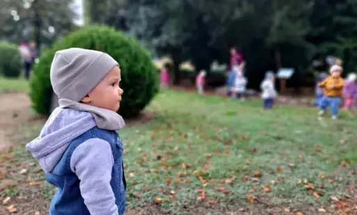Chłopczyk ubrany w czapkę i kurteczkę patrzy w dal, w tle inne dzieci
